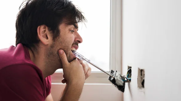worried-person-with-a-screwdriver-in-his-mouth-looking-at-a-malfunctioning-wall-socket
